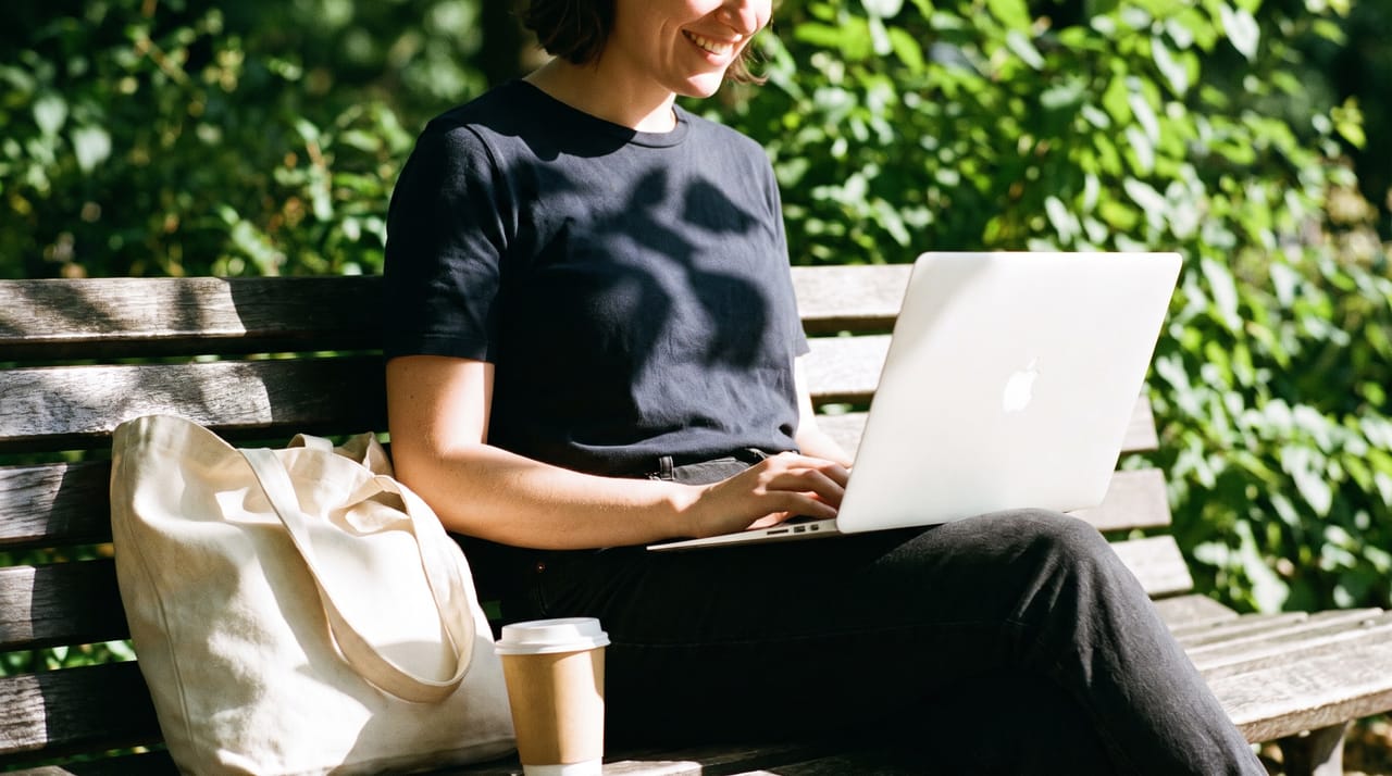 A laptop open on a park bench with a calendar on the screen and trees in the background